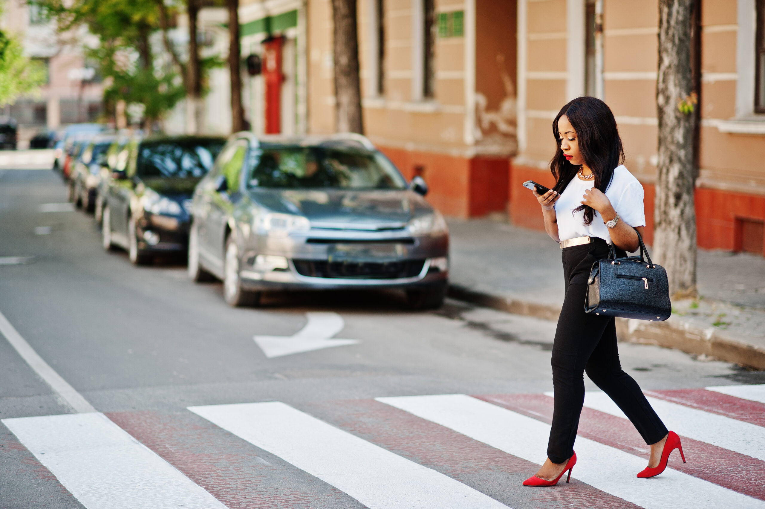 Stylish african american business woman on streets of city at pedestrian crossing.