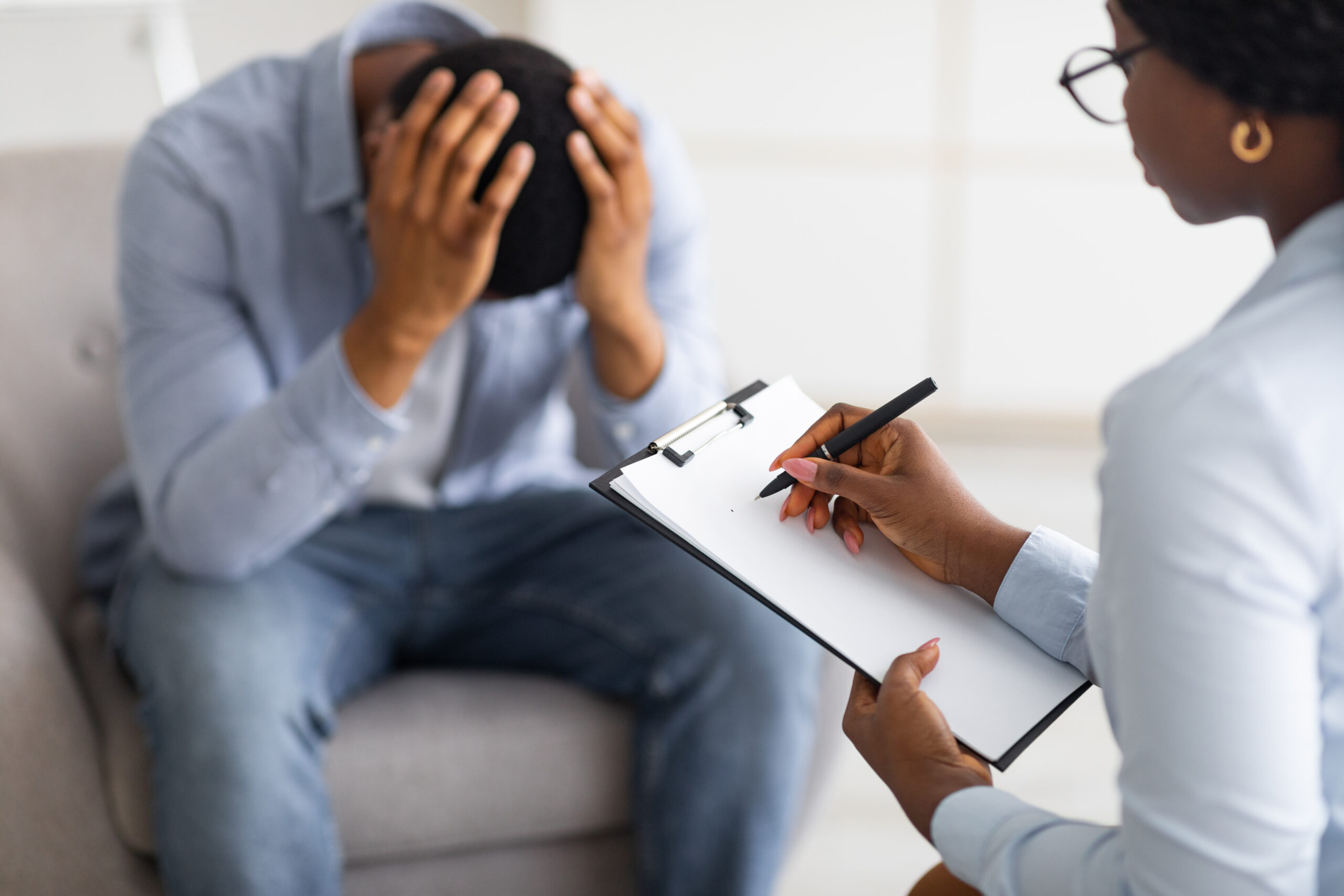 Depressed guy holding his head at counselor's office, seeking professional help with mental disorder